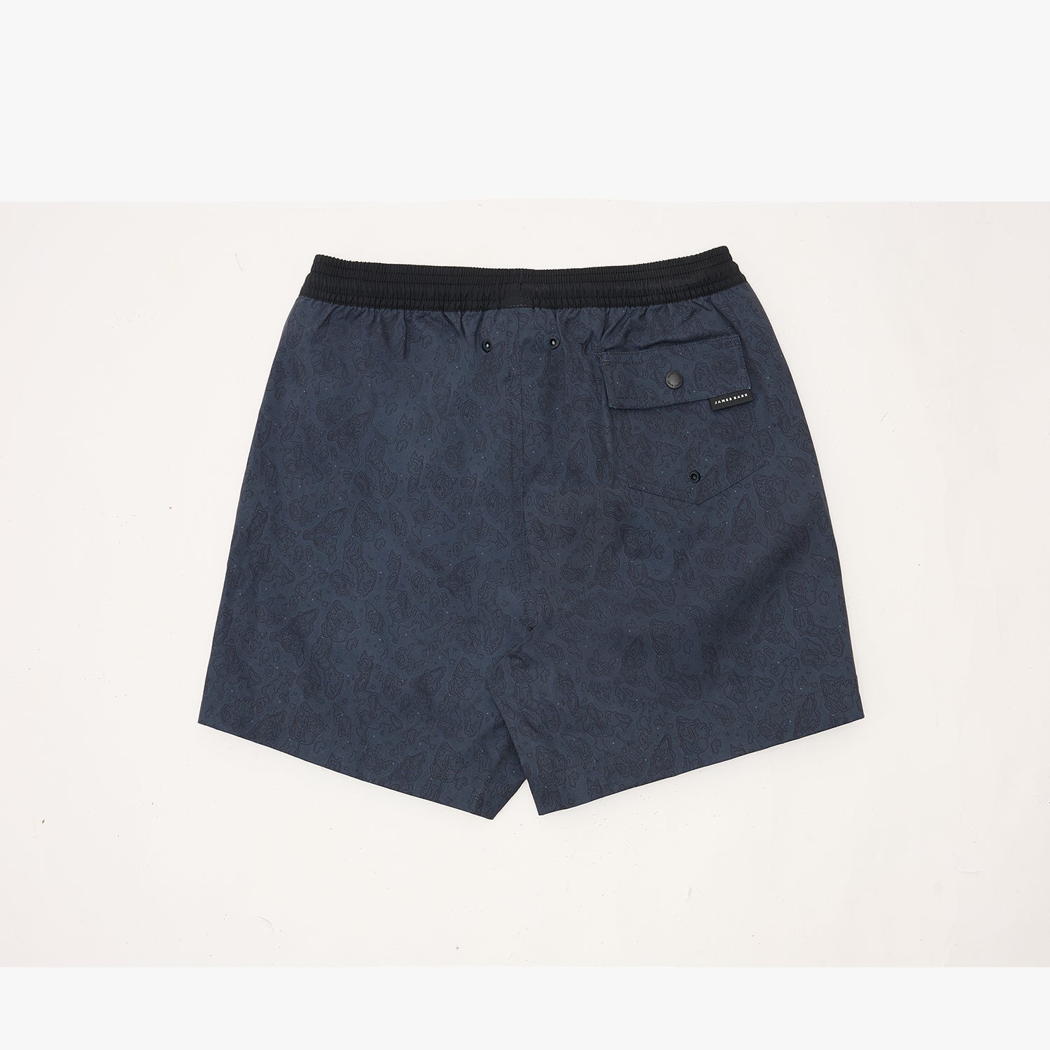 A pair of dark navy blue swim trunks with a subtle tonal pattern, featuring a black elastic waistband and a side pocket with a small black brand tag