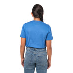 Rear view of a girl wearing the blue t-shirt, standing with her hands behind her back.
