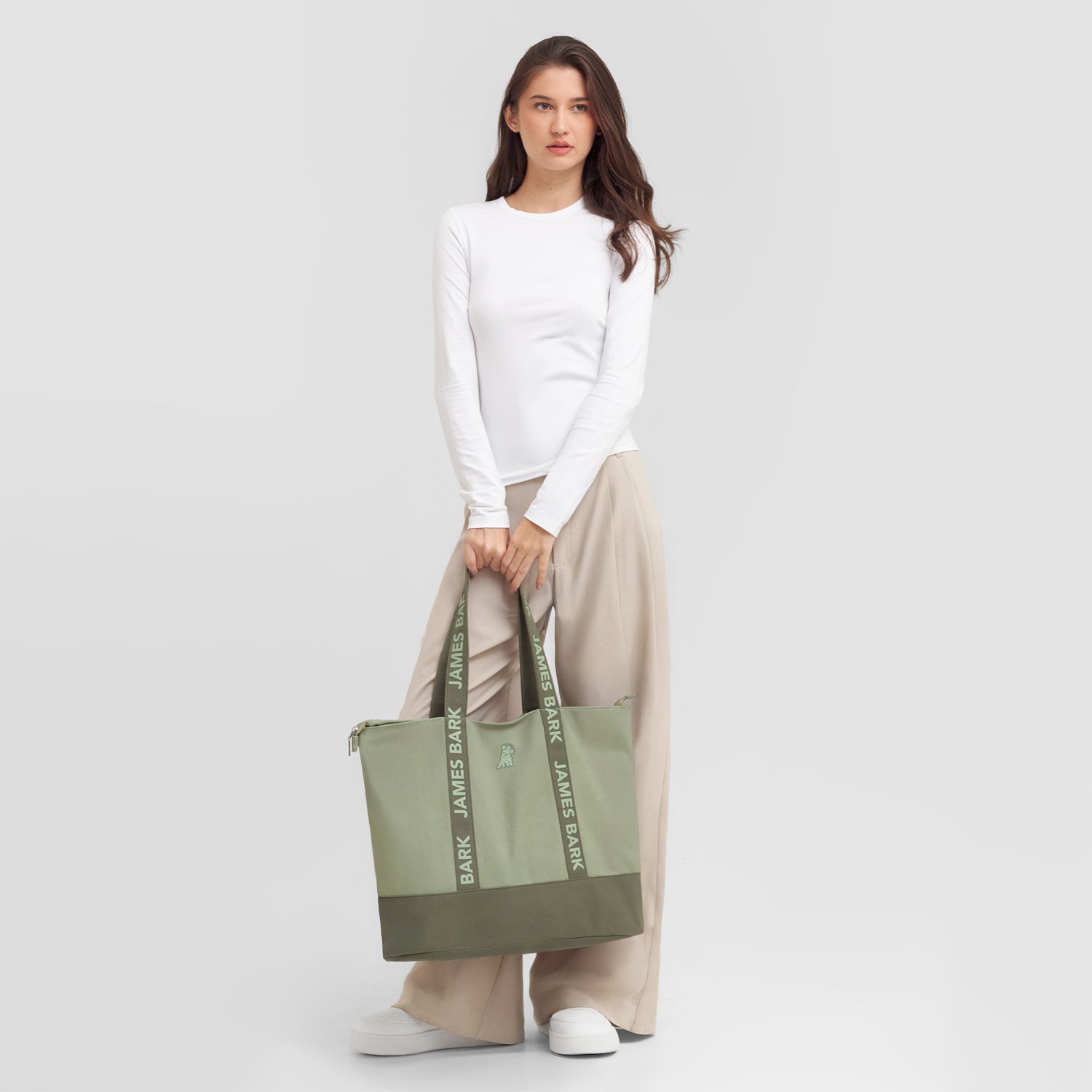 Woman holding a green tote bag with 'James Bark' branding against a white background