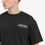 Close-up shot of the "JAMES BARK ELEMENTS" logo printed on the chest of the black t-shirt