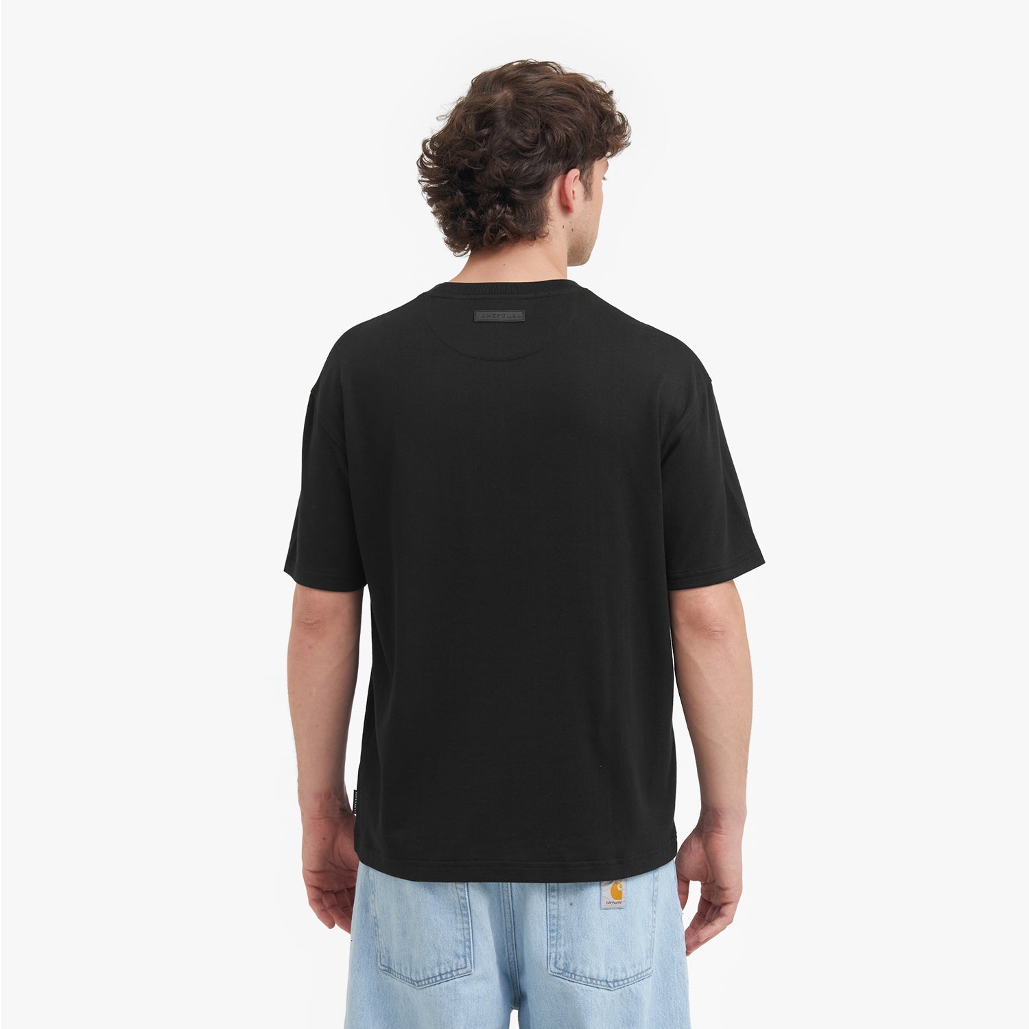 Back view of a man wearing a black t-shirt with a visible brand logo on the back, standing against a white background.