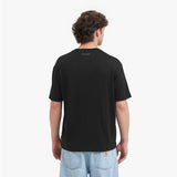 Back view of a man wearing a black t-shirt with a visible brand logo on the back, standing against a white background.