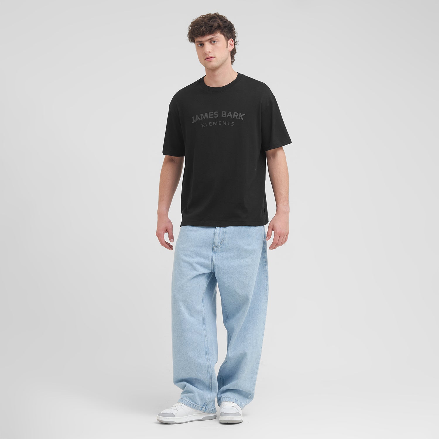 Man wearing a black t-shirt with 'James Bark' logo and light blue jeans on a white background