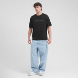 Man wearing a black t-shirt with 'James Bark' logo and light blue jeans on a white background