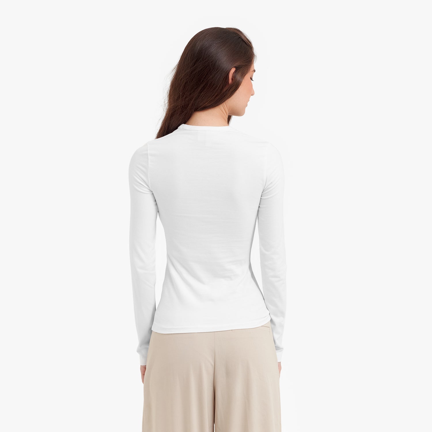Back view of a woman wearing a white long-sleeve top and beige pants on a white background