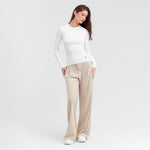 Woman wearing a white long-sleeve top and beige pants on a light gray background