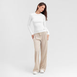 Woman wearing a white long-sleeve top and beige pants on a light gray background