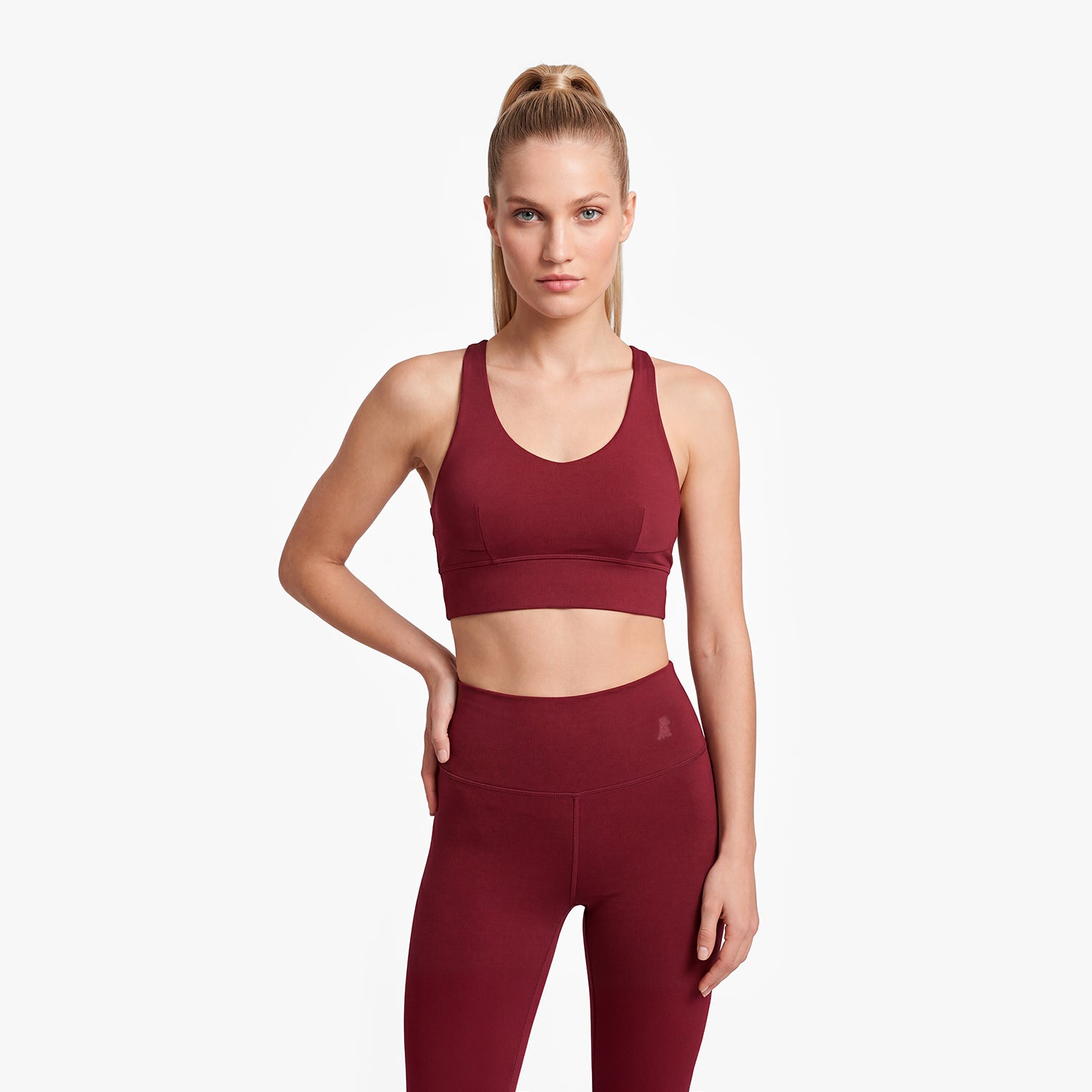 Woman wearing a maroon sports bra and leggings on a white background