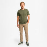 Man wearing a green t-shirt and beige pants on a white background
