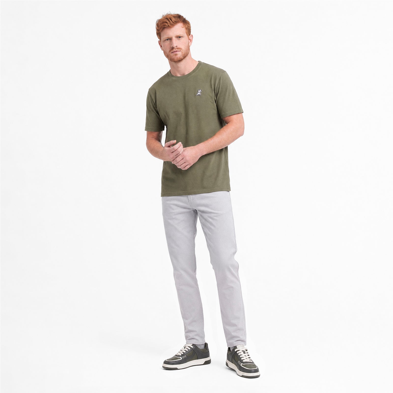 Man wearing a green t-shirt and light gray pants on a white background