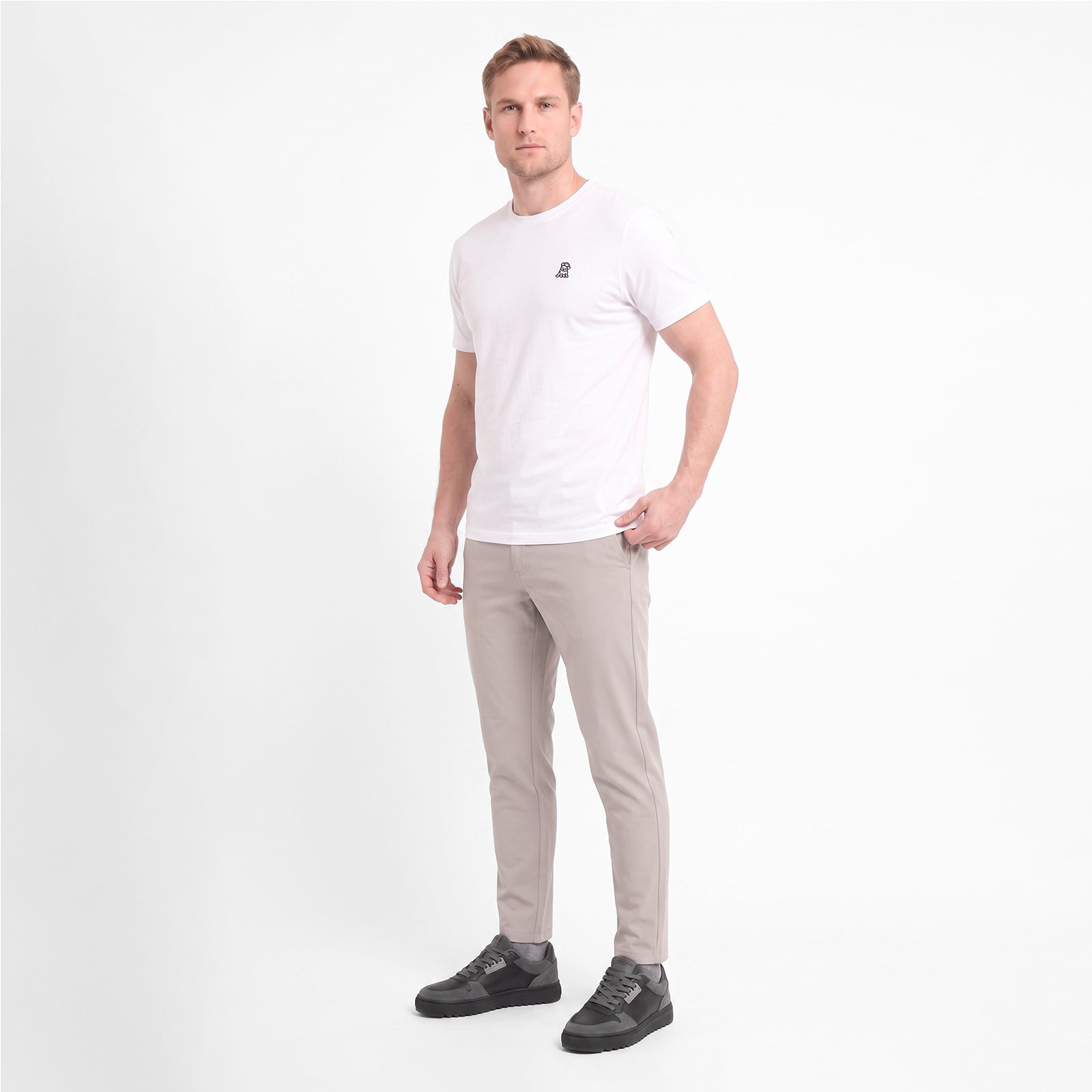 A man wearing a white short-sleeve crewneck t-shirt with a small black logo, paired with light gray trousers