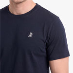A close-up of a man wearing a navy blue crew-neck t-shirt with a small white embroidered dog