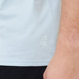 Light blue shirt with a logo on the chest worn by a person.