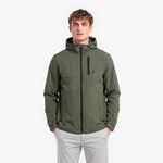 A man wearing an olive green hooded jacket with a black zipper and a small black logo on the chest, paired with light gray pants