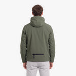 A man viewed from the back wearing an olive green hooded jacket with a black zippered pocket on the lower back, paired with light gray pants