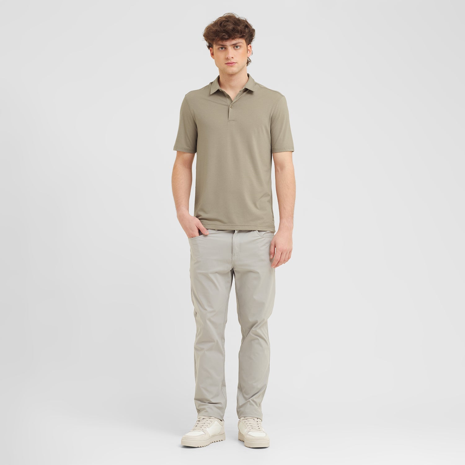 Man wearing a green polo shirt and light gray pants on a white background