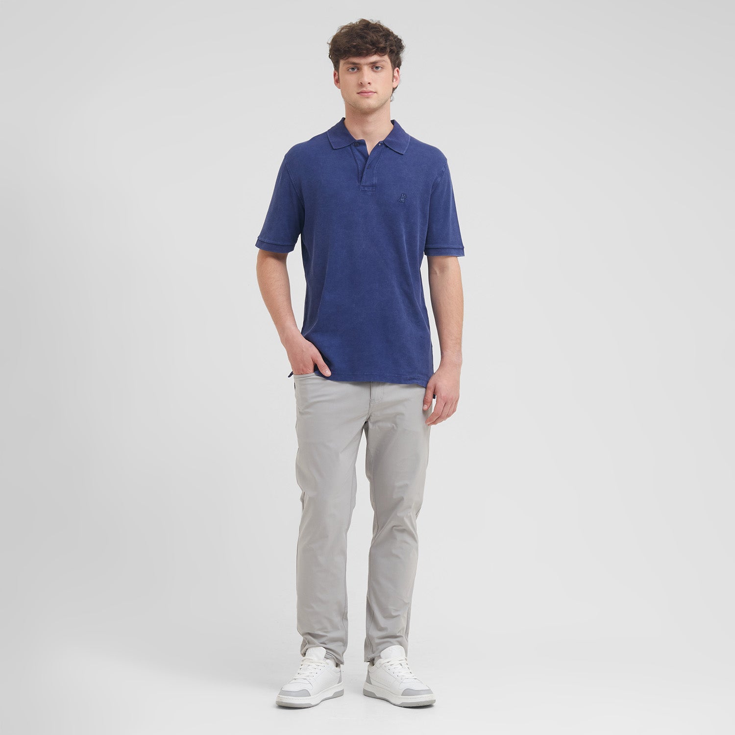 Man wearing a blue polo shirt and gray pants on a white background