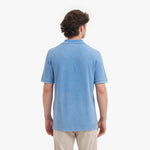 Back view of a man wearing a light blue polo shirt on a white background