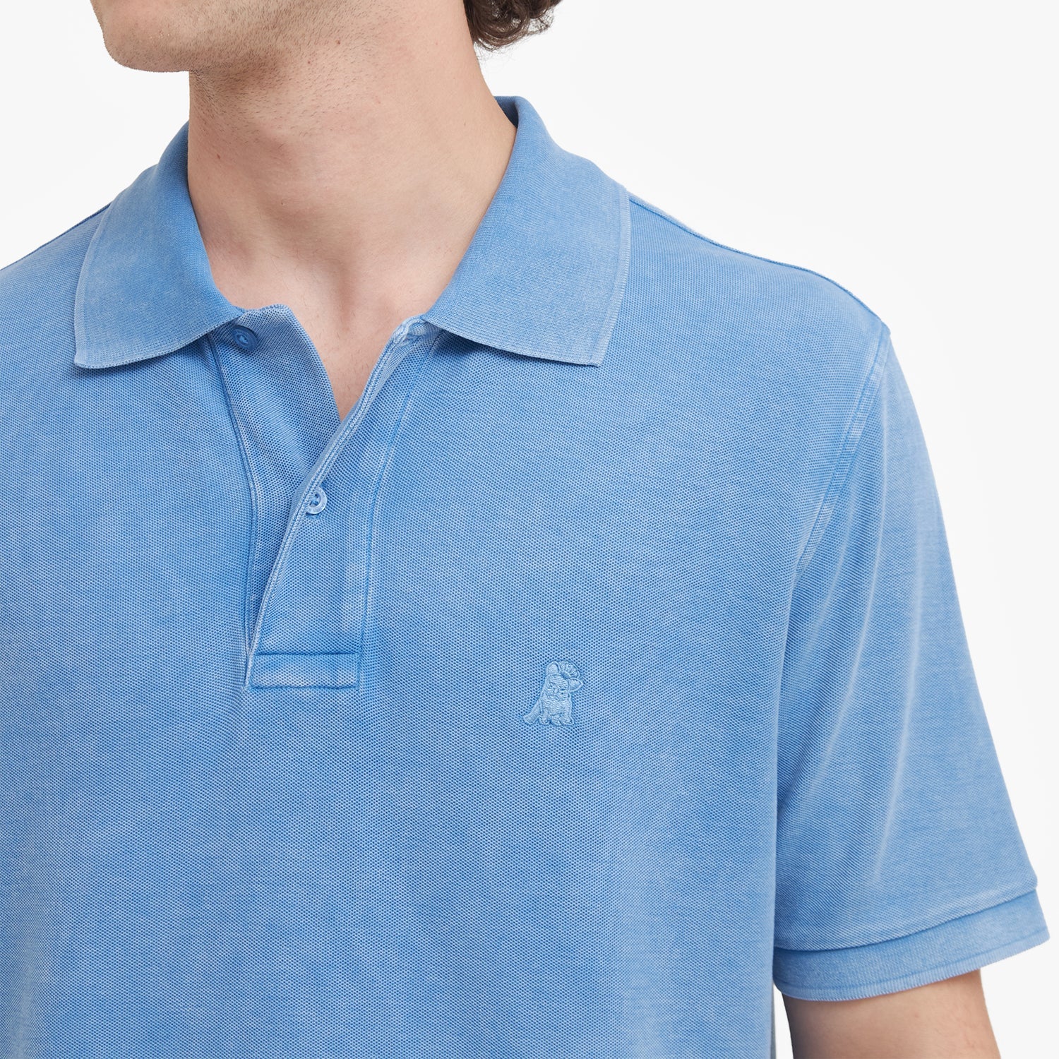 Close-up of a blue polo shirt with a small logo on a white background