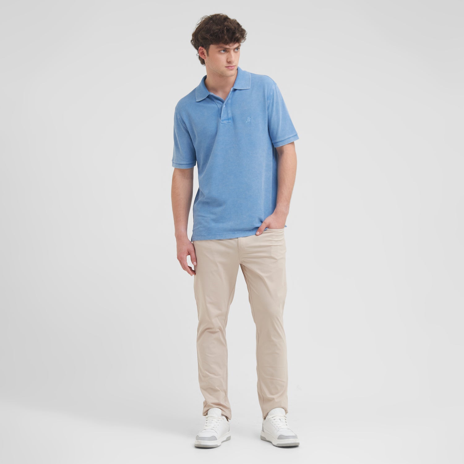 Man wearing a blue polo shirt and beige pants on a white background