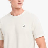 Person wearing a white t-shirt with a small logo on a plain background
