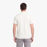A man viewed from the back wearing a short-sleeve polo shirt in off-white and gray trousers