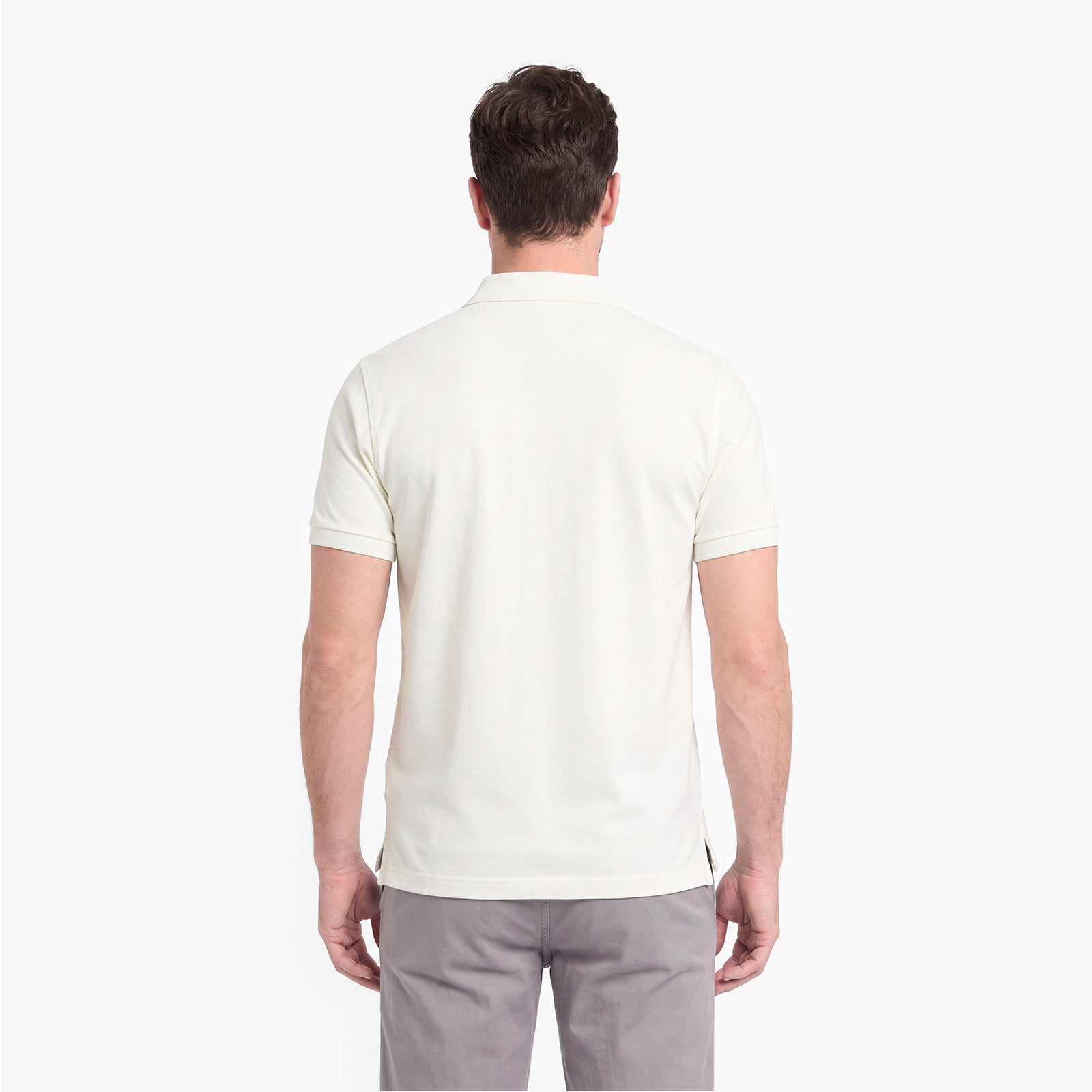 A man viewed from the back wearing a short-sleeve polo shirt in off-white and gray trousers