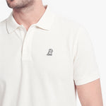 A close-up of a man wearing a white short-sleeve polo shirt with a small black embroidered dog logo on the left chest