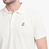 A close-up of a man wearing a white short-sleeve polo shirt with a small black embroidered dog logo on the left chest