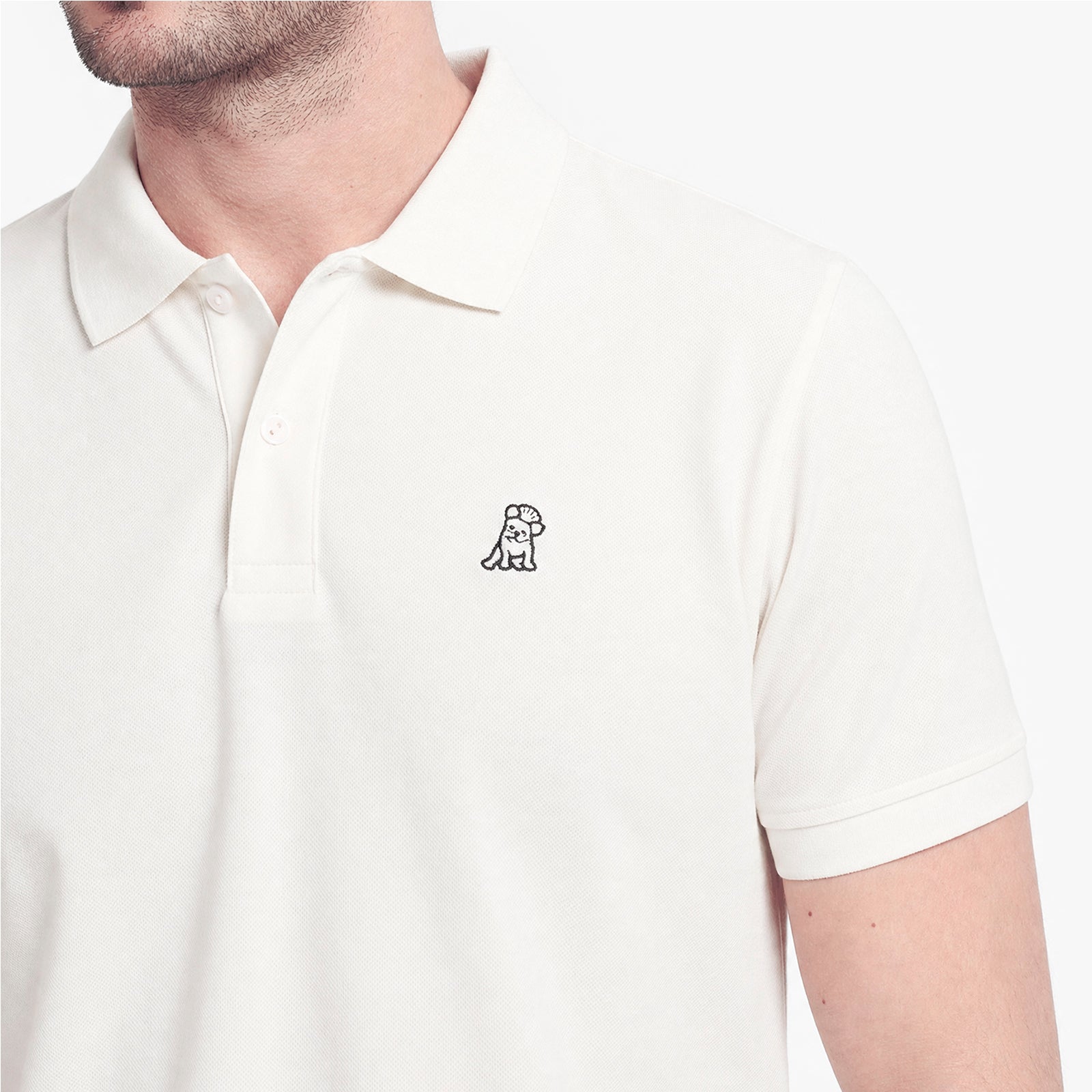 A close-up of a man wearing a white short-sleeve polo shirt with a small black embroidered dog logo on the left chest