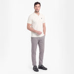 A man modeling a short-sleeve polo shirt in off-white with gray trousers and black shoes, standing against a plain white studio background.