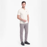 A man modeling a short-sleeve polo shirt in off-white with gray trousers and black shoes, standing against a plain white studio background.