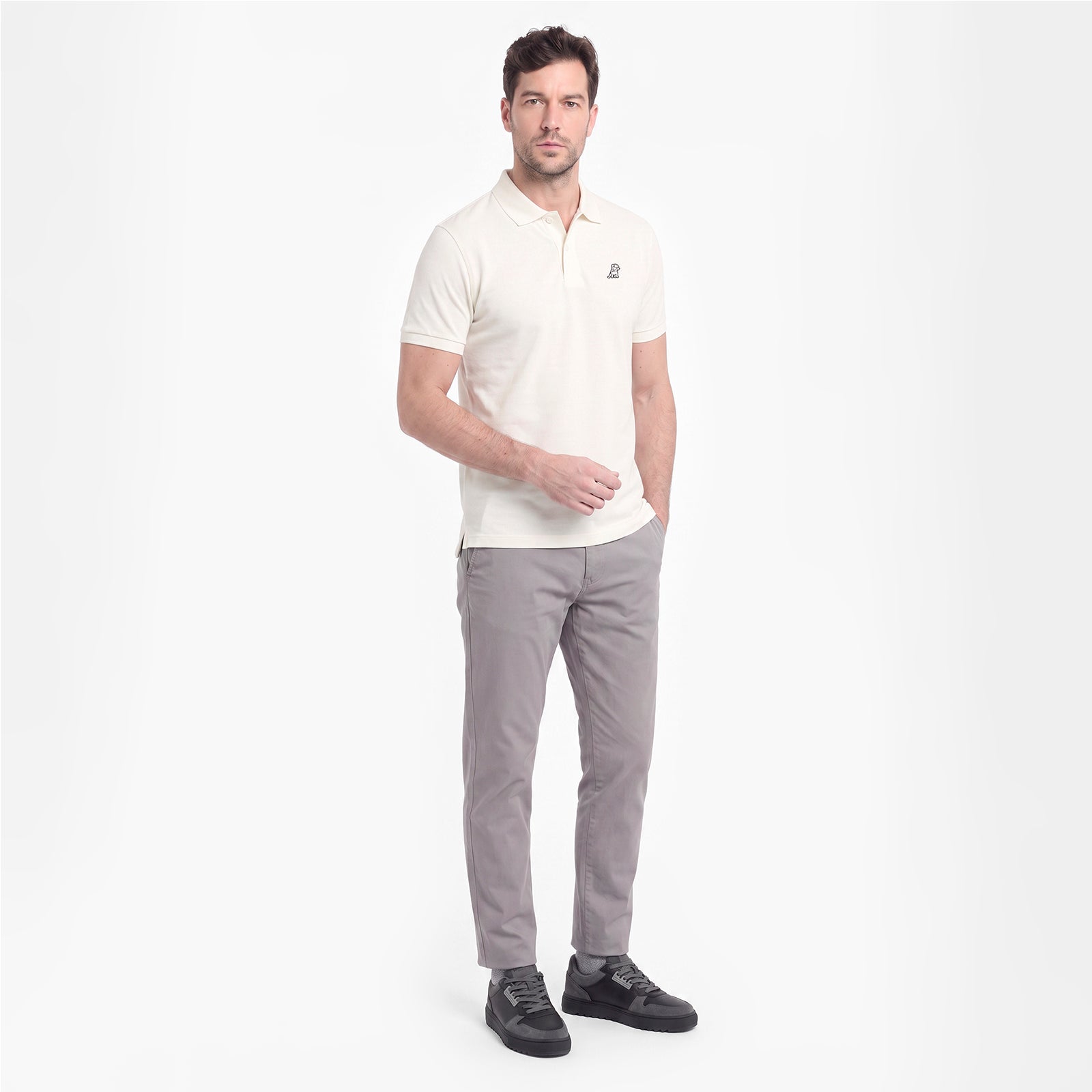 A man modeling a short-sleeve polo shirt in off-white with gray trousers and black shoes, standing against a plain white studio background.