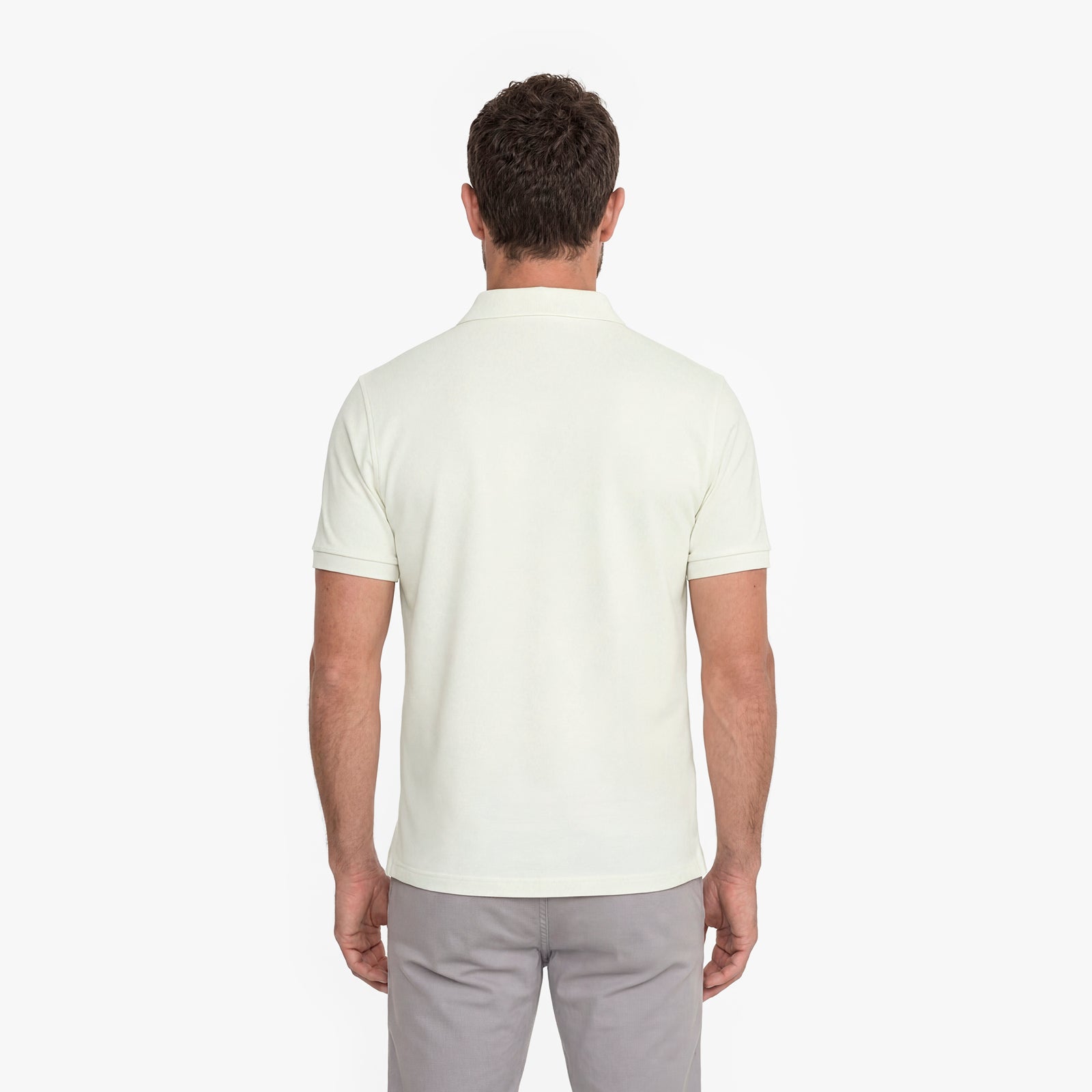 Man wearing a white polo shirt and light gray pants on a white background