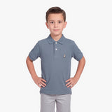 A young boy modeling a slate blue polo shirt with a small embroidered dog logo on the chest, paired with light gray pants, against a plain white background.