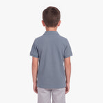 A child viewed from the back wearing a short-sleeve polo shirt in a muted slate blue color, paired with light gray pants, against a plain white background.