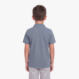 A child viewed from the back wearing a short-sleeve polo shirt in a muted slate blue color, paired with light gray pants, against a plain white background.