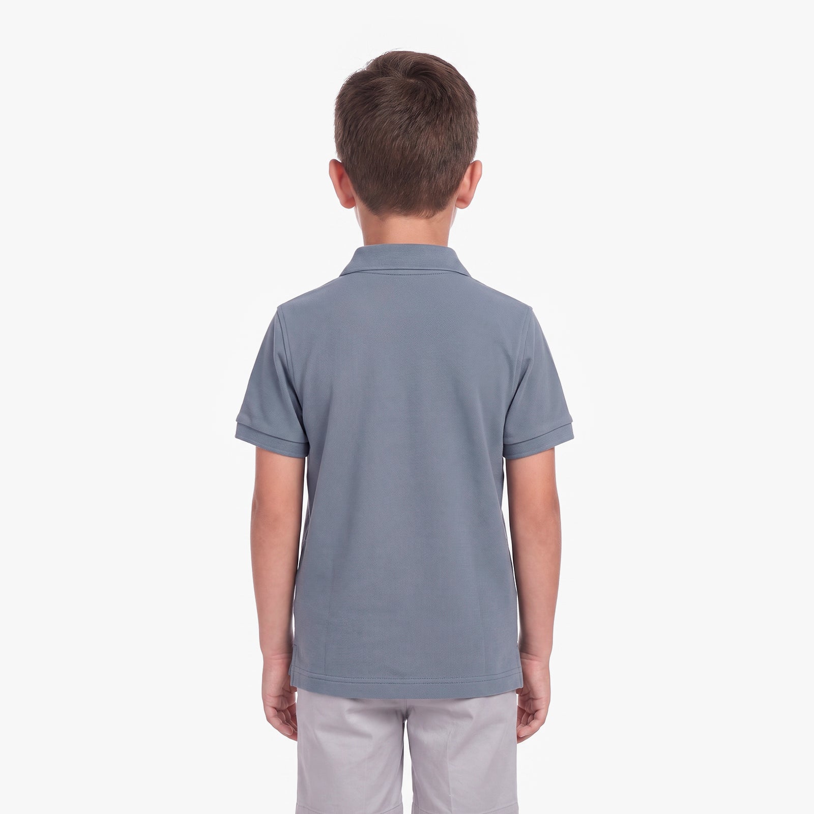 A child viewed from the back wearing a short-sleeve polo shirt in a muted slate blue color, paired with light gray pants, against a plain white background.