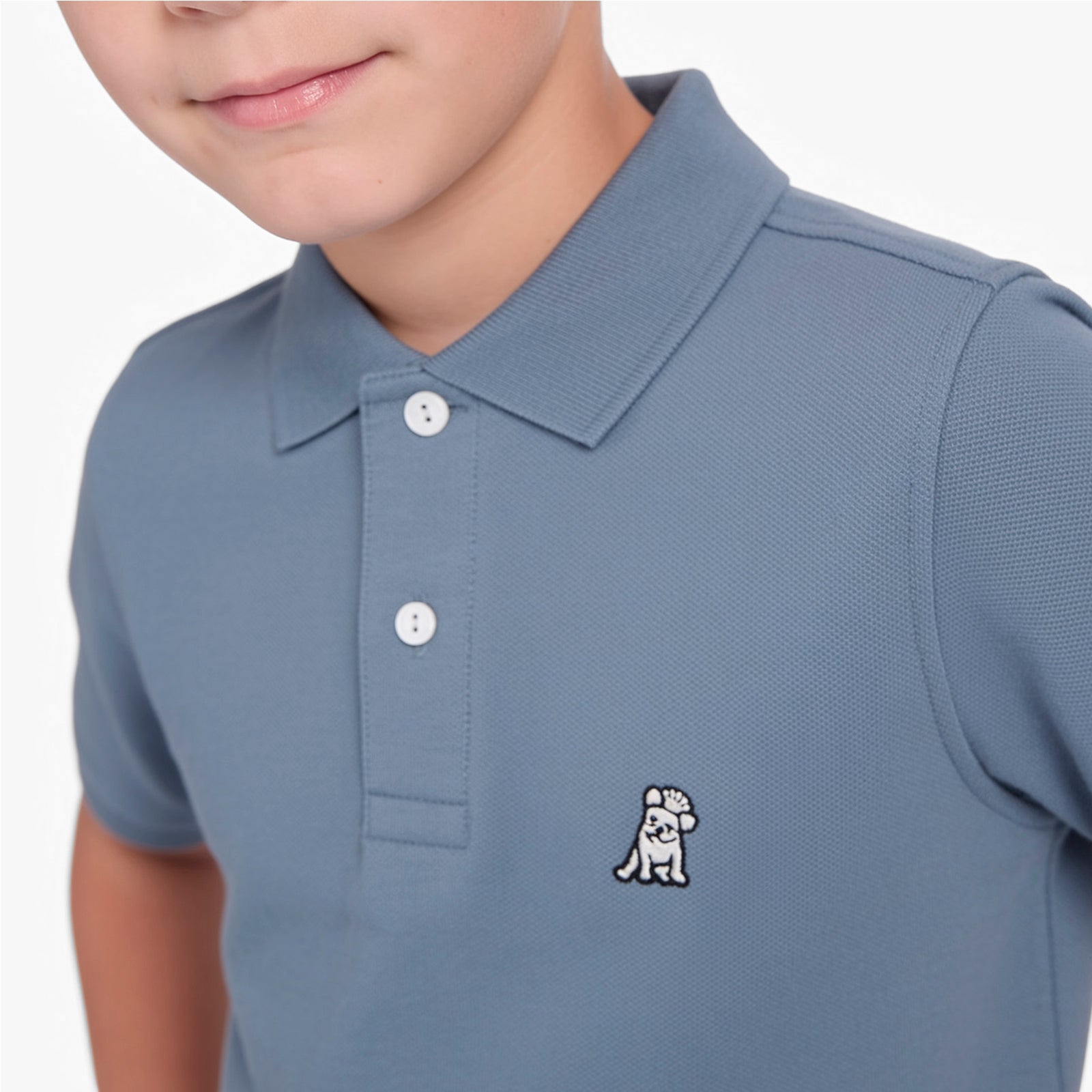 Close-up of a child wearing a dusty slate blue polo shirt with a small embroidered dog logo on the left chest, set against a clean white background.