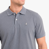A close-up of a man wearing a gray short-sleeve polo shirt with a small embroidered dog logo on the chest
