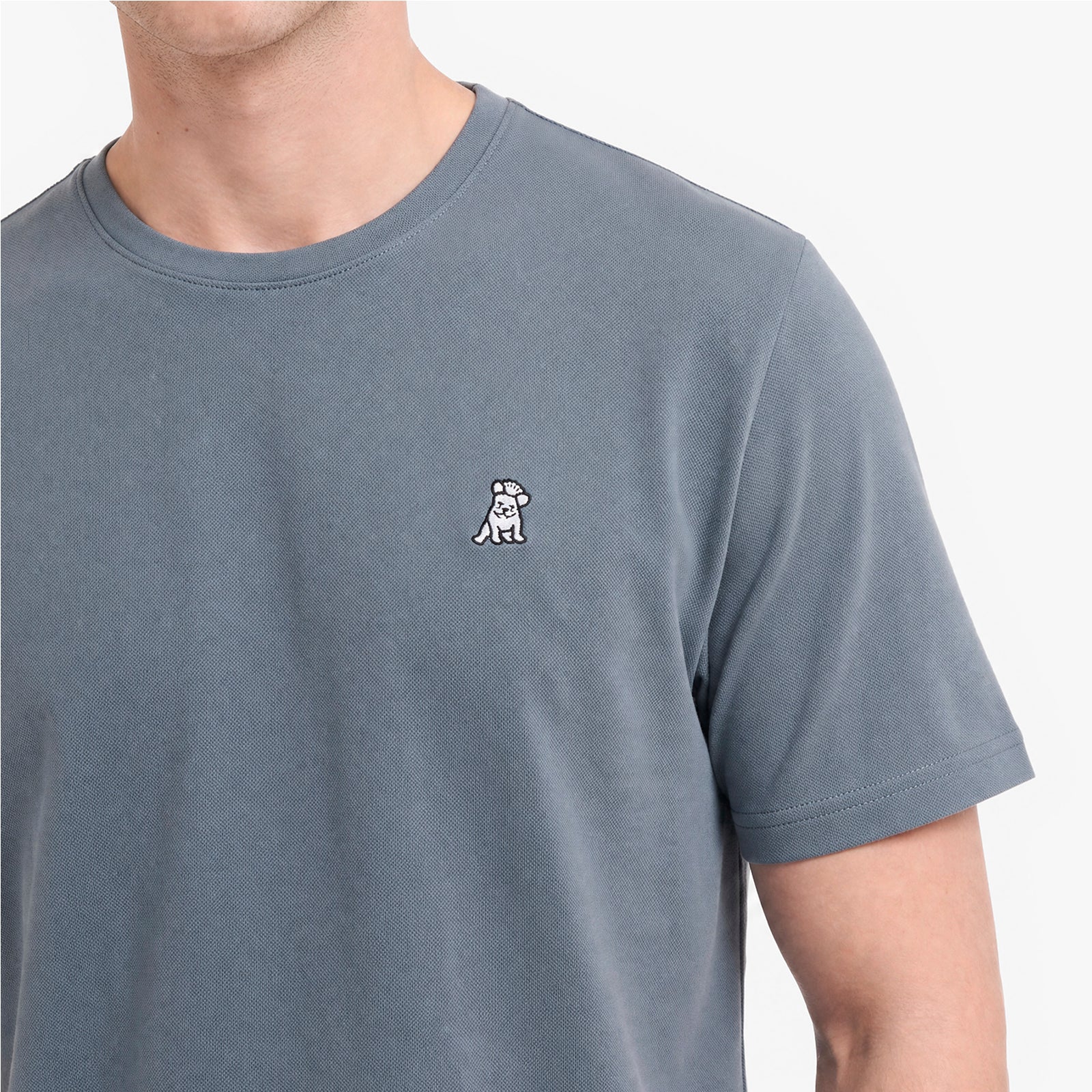 A close-up of a person wearing a slate blue crewneck t-shirt with a small white embroidered dog logo