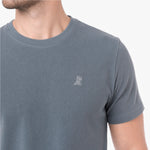 A close-up of a man wearing a slate gray crew-neck t-shirt with a small white embroidered dog logo