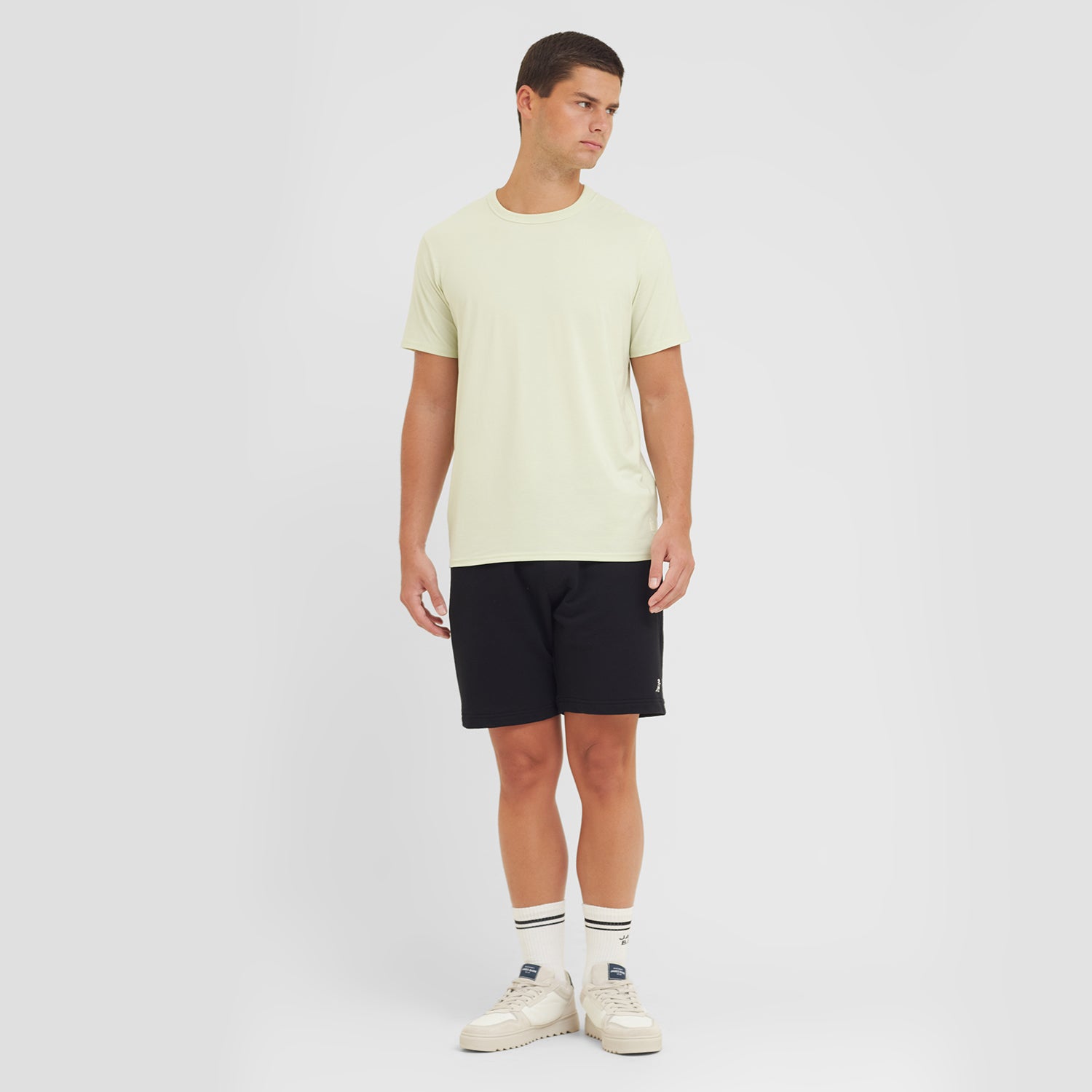 Man wearing a light yellow t-shirt and black shorts on a white background