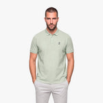 Man wearing a light green polo with a white embroidered logo on a white background