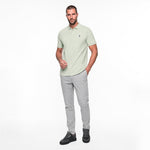 Man wearing a light green polo shirt and gray pants on a white background