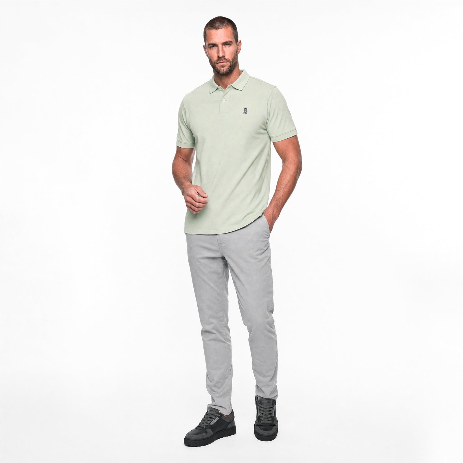 Man wearing a light green polo shirt and gray pants on a white background