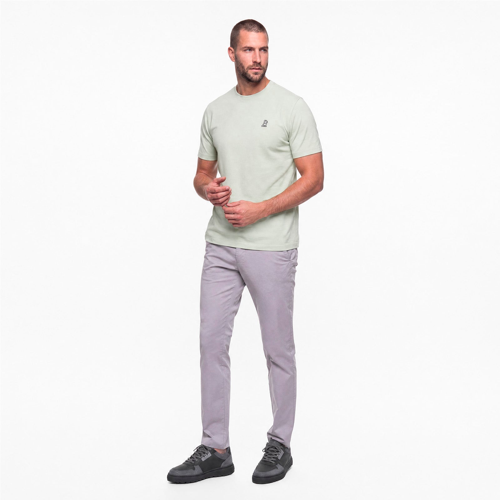 Man wearing a light green t-shirt and gray pants on a white background