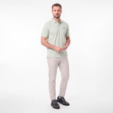 A man modeling a light sage green short-sleeve polo shirt with beige trousers and black shoes