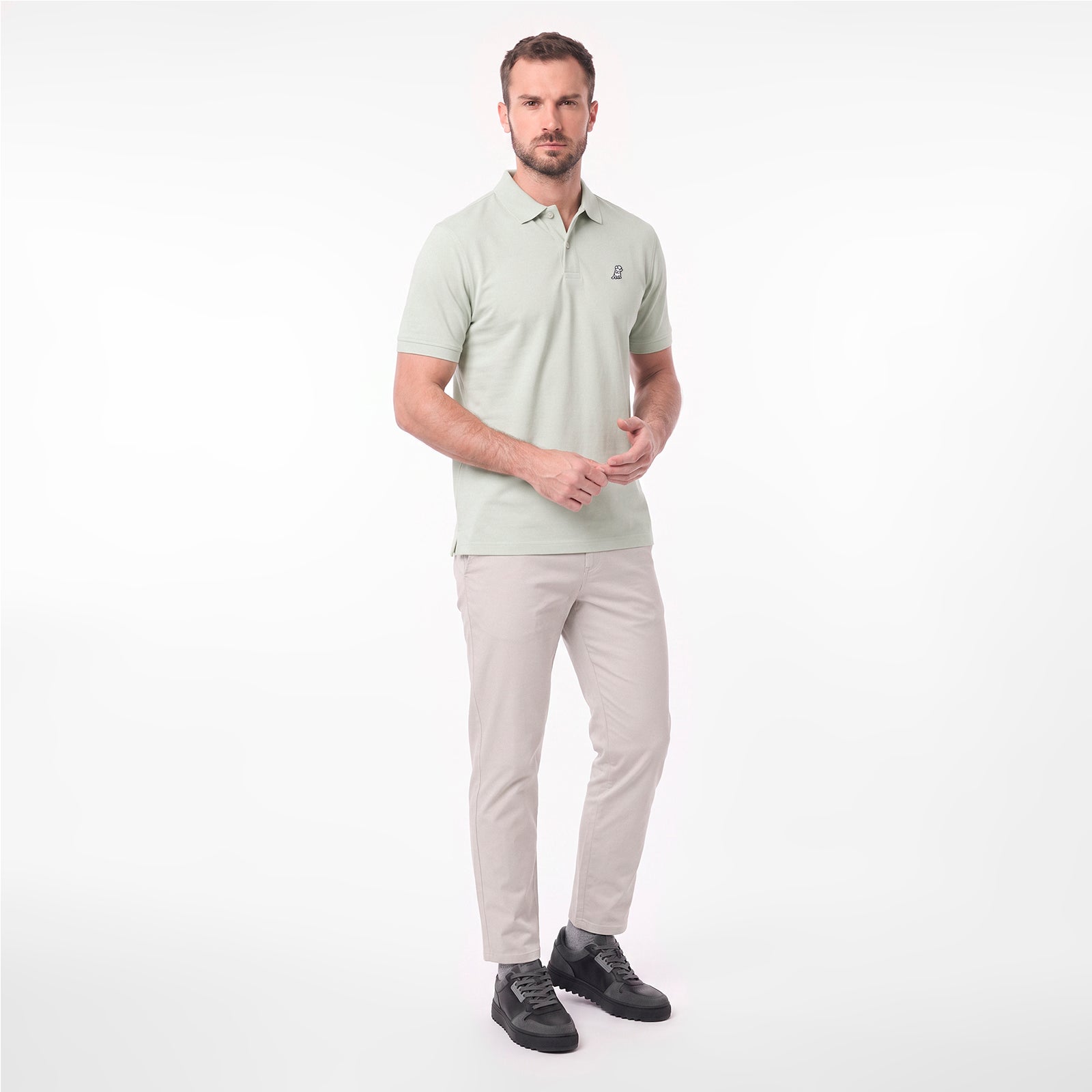 A man modeling a light sage green short-sleeve polo shirt with beige trousers and black shoes
