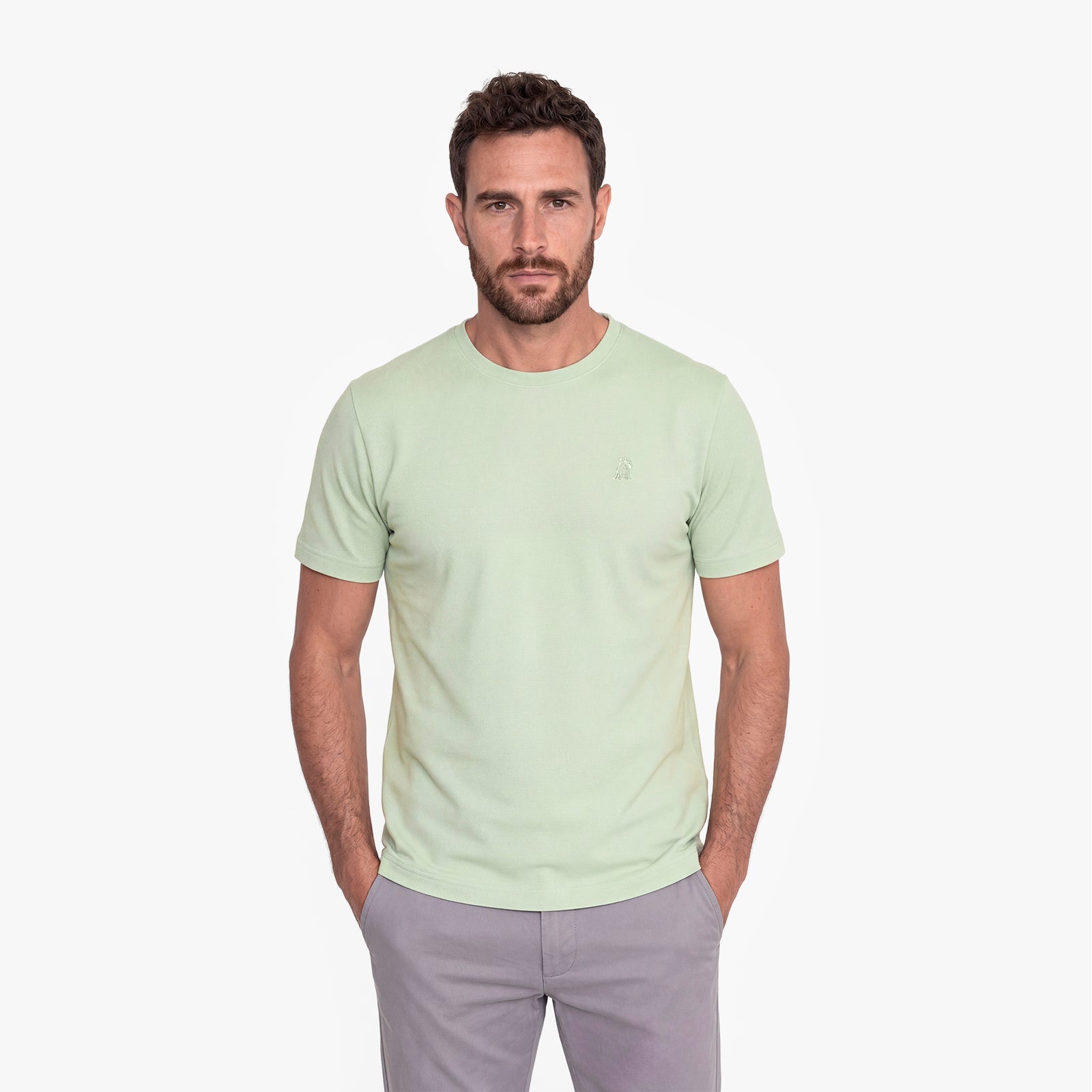 Man wearing a light green t-shirt and gray pants on a white background